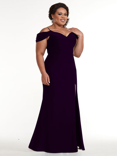 A woman models Avery Austin's 83029: a deep purple, floor-length off-the-shoulder gown with a thigh-high slit, standing against a white background and smiling gently with one hand on her shoulder.