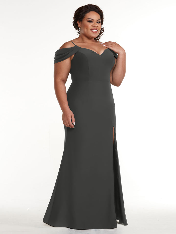 A woman smiles against a plain white background, wearing Avery Austin style 83029—a floor-length, off-the-shoulder dark gray fitted dress with a sweetheart neckline and thigh-high slit.