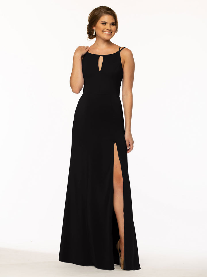 A woman smiles against a white background wearing Avery Austin’s 83030—a sleeveless, floor-length black sheath dress with a bateau neck, front keyhole cutout, and high slit.