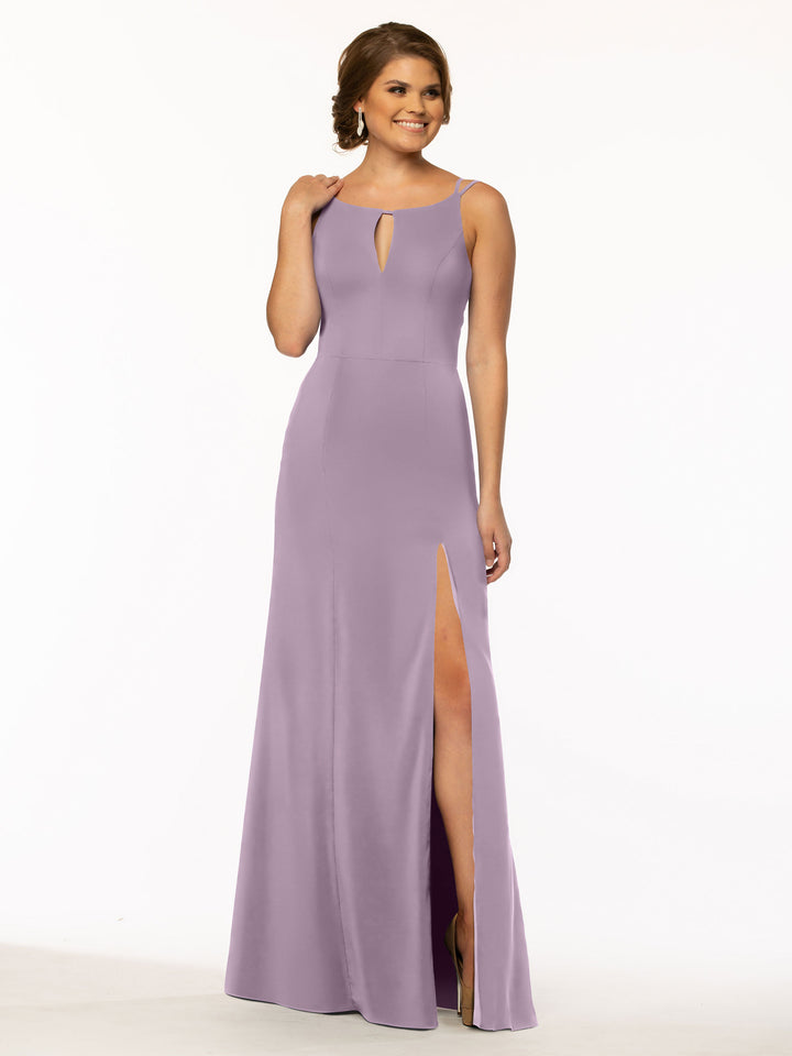 A woman wearing Avery Austin 83030, a sleeveless floor-length sheath dress in lavender with a front keyhole and high slit skirt, stands smiling against a white background, touching her hair.