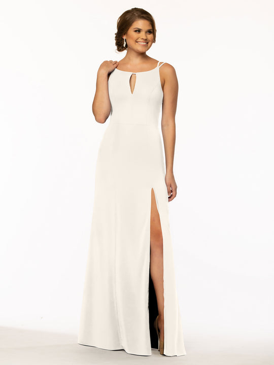 A woman stands smiling against a plain white background, wearing the Avery Austin 83030: a sleeveless, floor-length white sheath dress with a thigh-high slit and keyhole neckline.