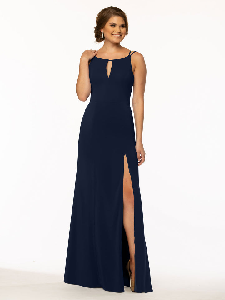 A woman wearing Avery Austin’s 83030, a sleeveless floor-length sheath dress in navy with a thigh-high slit and keyhole neckline, smiles against a plain white background.