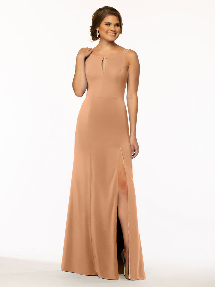 A woman smiles against a white background, wearing Avery Austin’s 83030: a sleeveless, floor-length peach sheath dress with a keyhole neckline and high slit skirt.