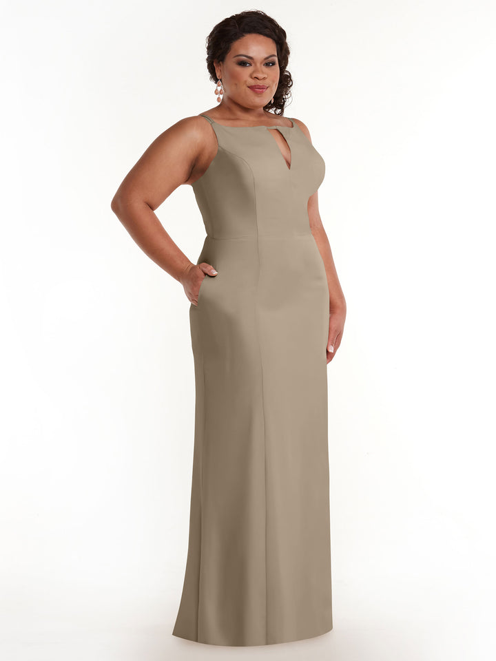A woman poses with one hand in her pocket against a white background, wearing the Avery Austin 83030 sleeveless taupe floor-length sheath dress featuring a keyhole neckline and side pockets.