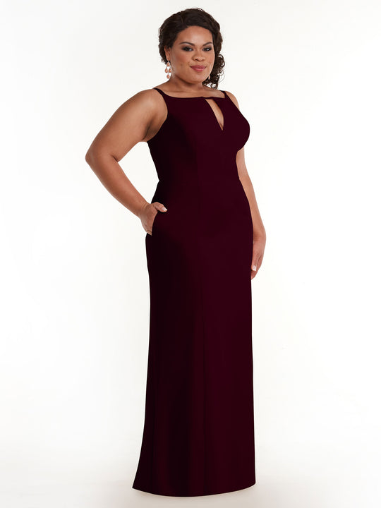A woman wears the Avery Austin TH-83030, a sleeveless maroon sheath dress with a keyhole neckline and side slit, standing with hands in pockets and smiling slightly against a plain white background.