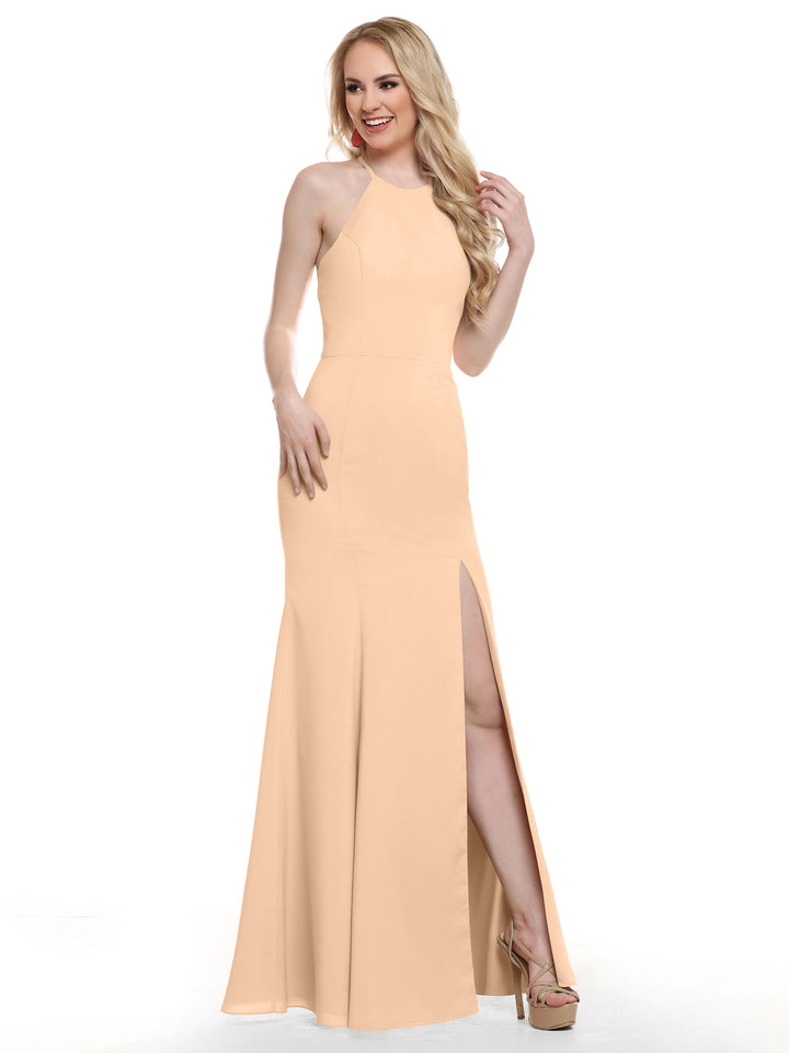 A woman with long blonde hair smiles in Avery Austin style 83031, a sleeveless peach fitted dress featuring a high neckline, strappy back, and thigh-high slit. She stands against a white background wearing high heels.