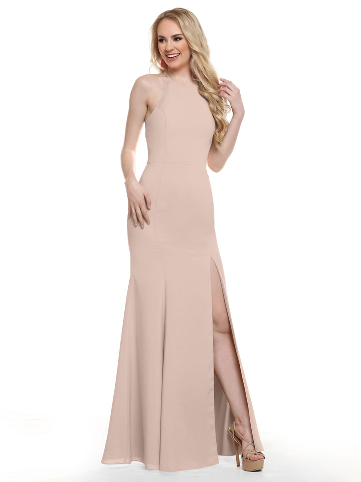 A woman stands smiling, one hand in her long wavy blonde hair, wearing Avery Austin’s 83031—a sleeveless, floor-length rose pink halter dress with a high neckline and thigh-high slit.