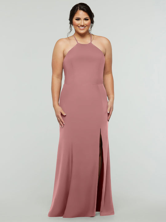A woman smiles against a light gray background wearing Avery Austin's TH-83031, a sleeveless blush pink fitted gown with a strapped back, high neckline, and front slit.