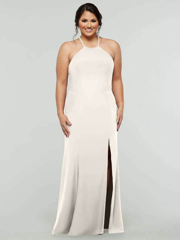 A woman stands and smiles against a plain light gray background, wearing Avery Austin style 83031—a sleeveless, floor-length white halter dress with a high neckline and thigh-high slit.