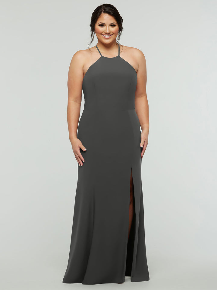 A woman models Avery Austin’s 83031: a sleeveless, floor-length dark gray halter dress with a fitted silhouette, front slit, and strapped back, smiling against a plain light gray background.