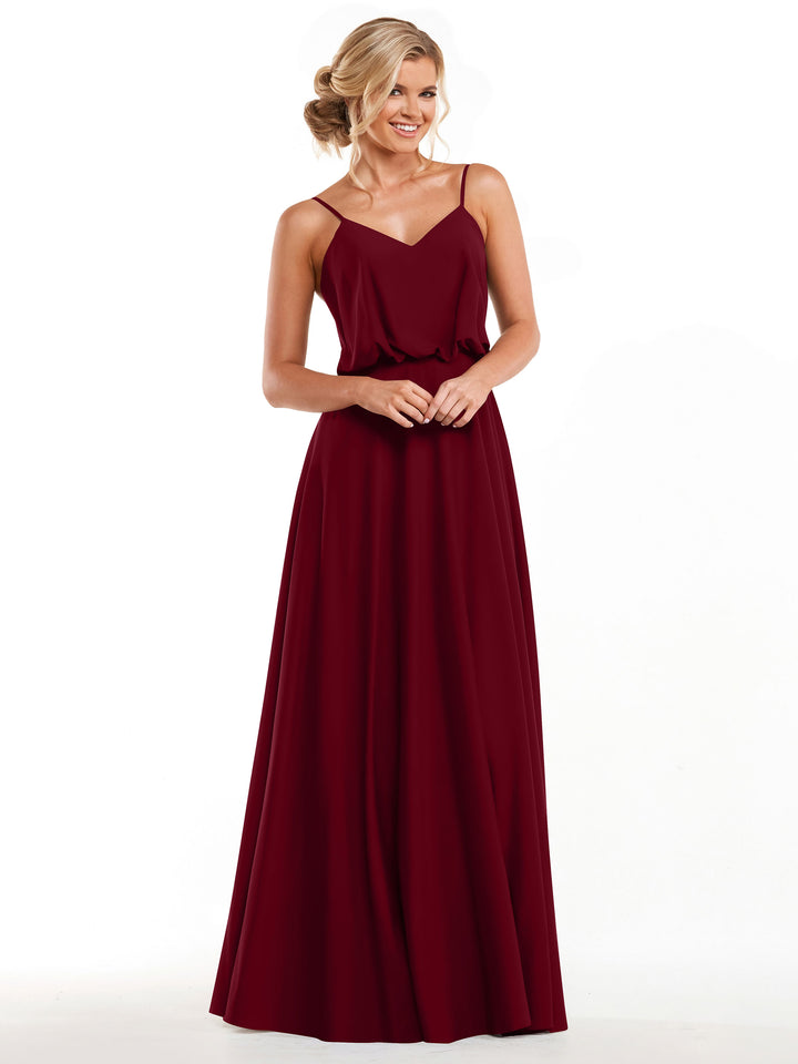 A woman stands smiling with her hands clasped, modeling the Avery Austin 83040: a sleeveless A-Line floor-length burgundy gown with thin straps and a flowy skirt, set against a plain white background.