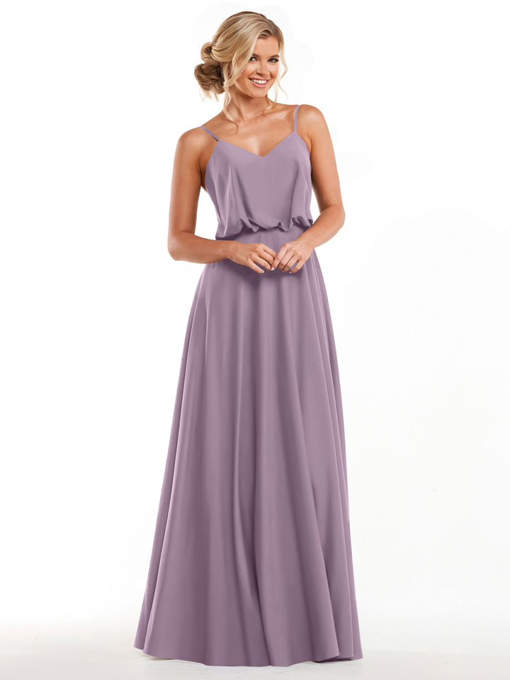 A woman with blonde hair in an elegant updo smiles as she wears Avery Austin style 83040—a floor-length, sleeveless lavender A-line dress featuring spaghetti straps and a loose-fitting V-neck bodice. Her hands are gently clasped.
