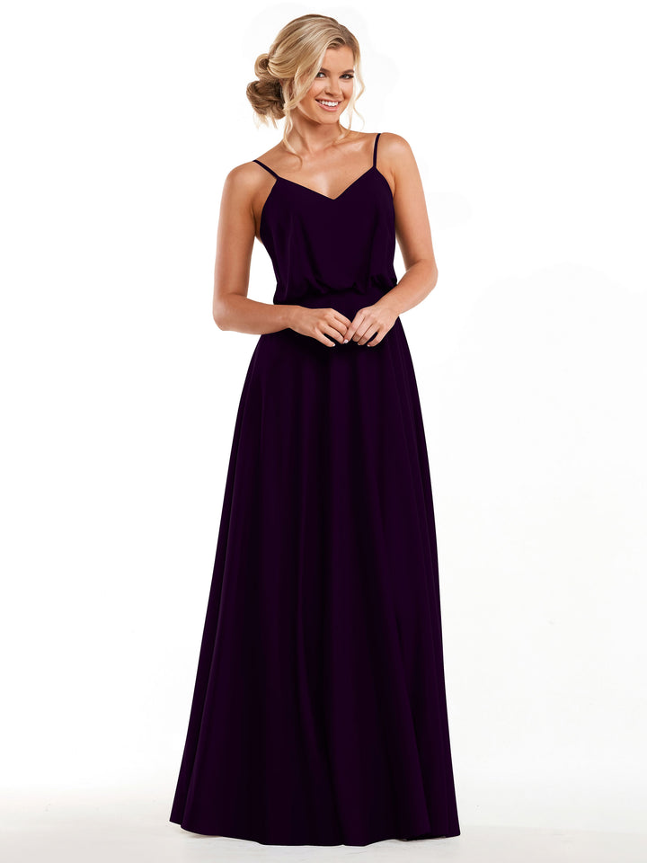 Model wearing Avery Austin 83040, a long dark purple A-line dress with thin straps and flowy skirt, stands against a white background. Her hair is in an elegant updo and she smiles with her hands gently clasped.