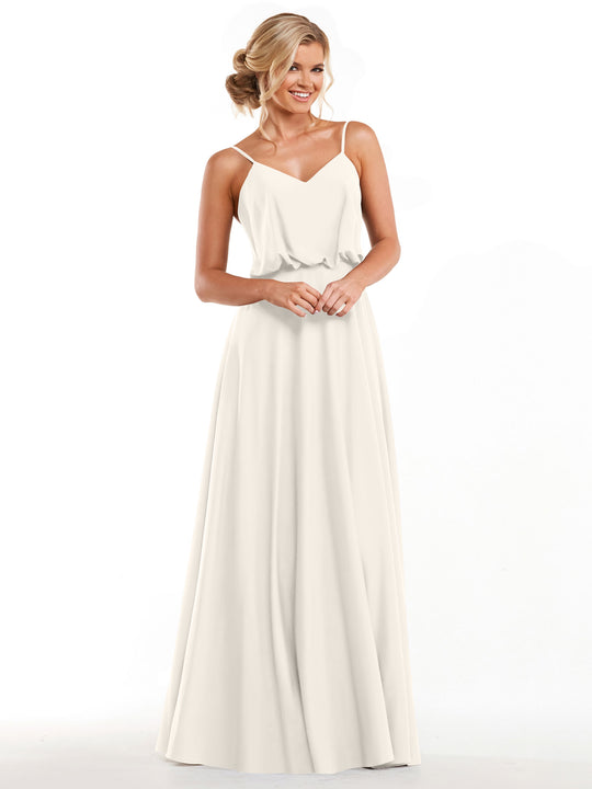 A woman stands smiling against a plain white background, wearing the Avery Austin 83040: a sleeveless, floor-length ivory A-line dress with thin straps, a relaxed bodice, and a fitted waist.