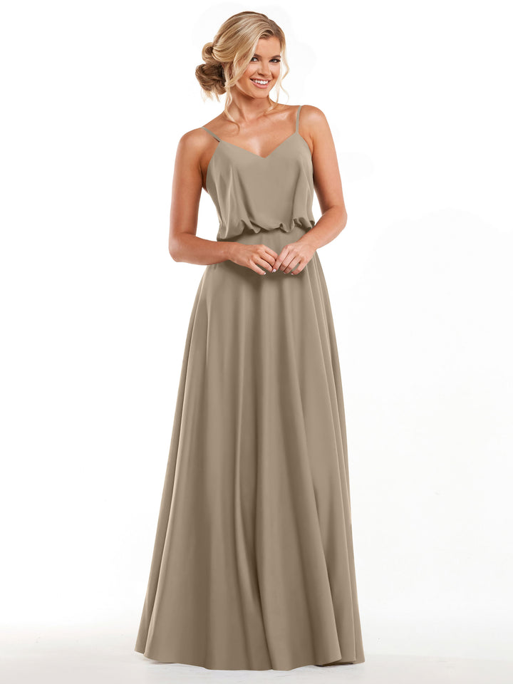 A woman in Avery Austin style 83040, a long taupe A-line dress with thin straps and a fitted waist, smiles against a white background with her hair in a loose updo.