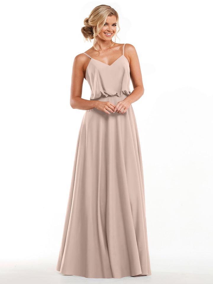 A woman stands smiling against a white background, hands clasped, wearing Avery Austin’s rose pink sleeveless A-Line dress (Style 83040) with spaghetti straps and a flowy skirt.