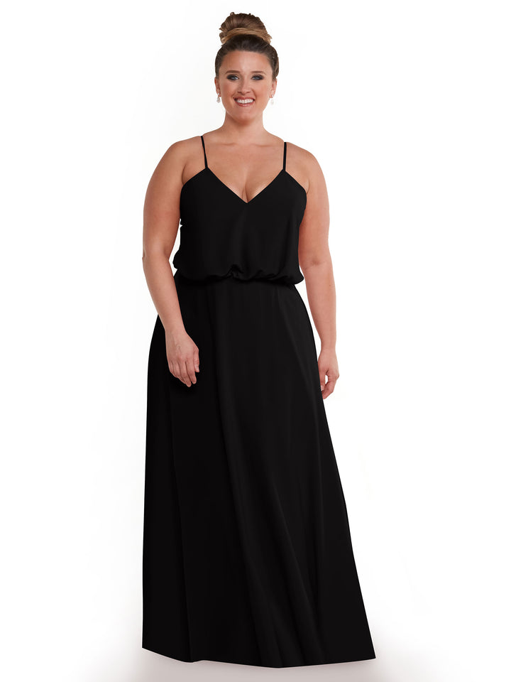 A woman with light skin and brown hair in a bun wears Avery Austin style 83040—a sleeveless, floor-length black A-line dress with spaghetti straps and a V-neck—while standing and smiling against a plain white background.