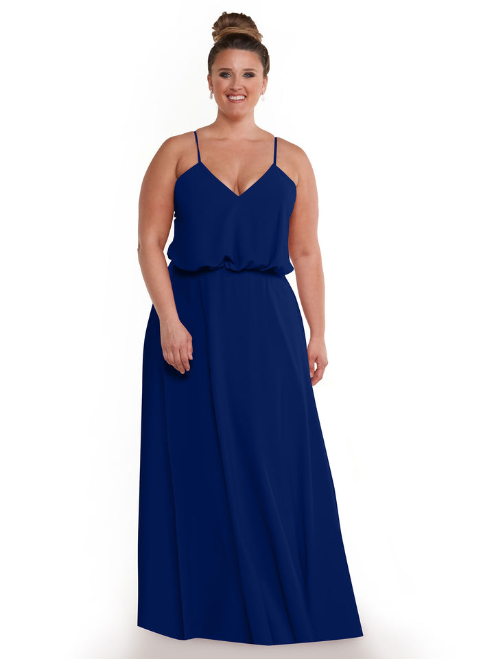 A woman with brown hair in a bun wears the Avery Austin 83040, a floor-length sleeveless royal blue A-line dress with thin straps and a V-neckline, standing and smiling against a white background.
