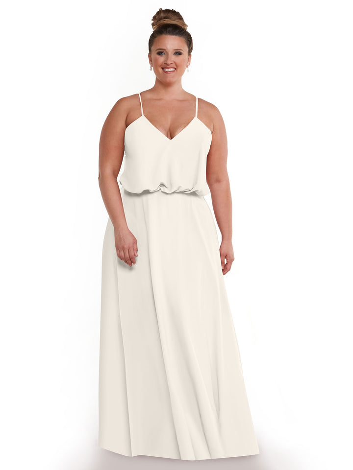 A smiling woman with brown hair in a bun models Avery Austin’s 83040, an A-line dress with thin straps, flowy skirt, and loose-fit bodice, standing against a plain white background.