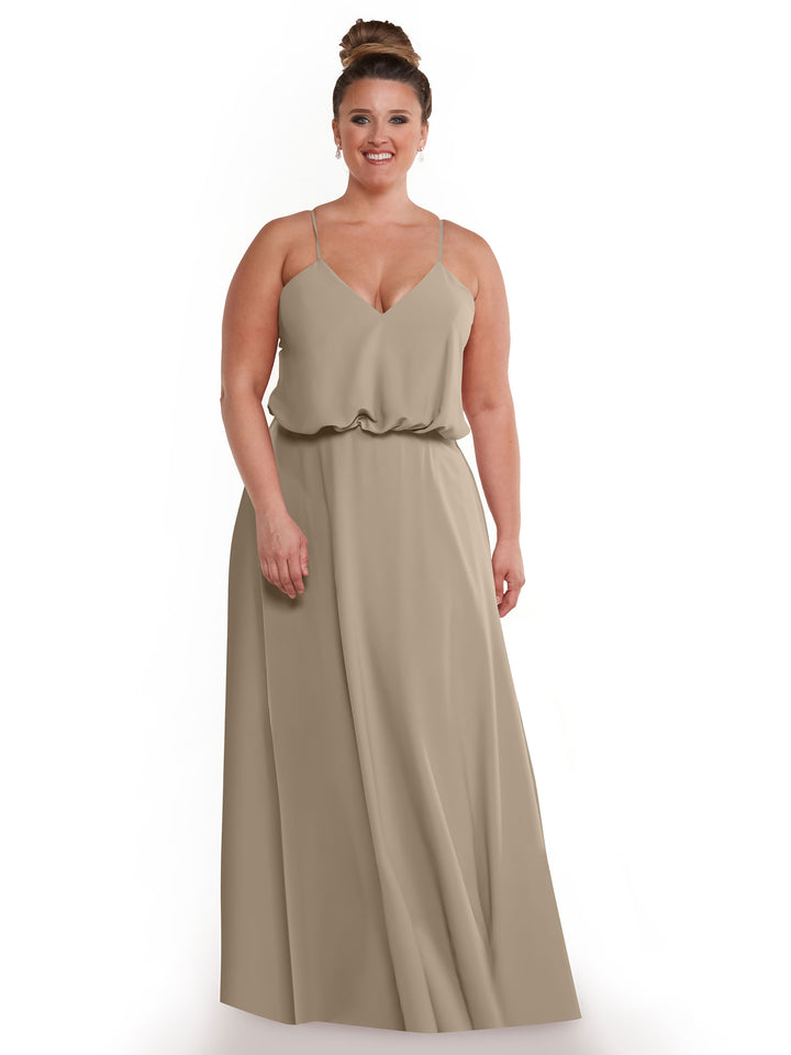 A woman with light skin and brown hair in a bun is wearing Avery Austin’s 83040 sleeveless, floor-length taupe A-line dress with thin straps and a blouson waist, smiling against a white background as the flowy skirt moves gracefully.