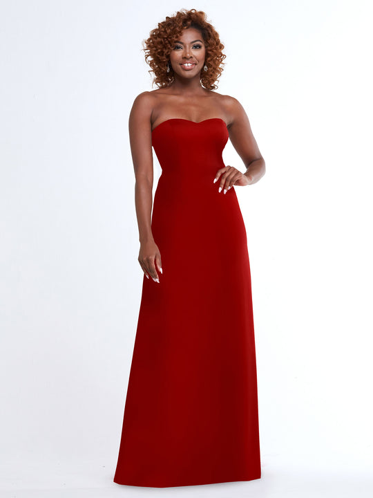 A woman with curly hair smiles against a white background, modeling the Avery Austin 83044 dress in Ruby—a strapless sweetheart gown with an A-line skirt.