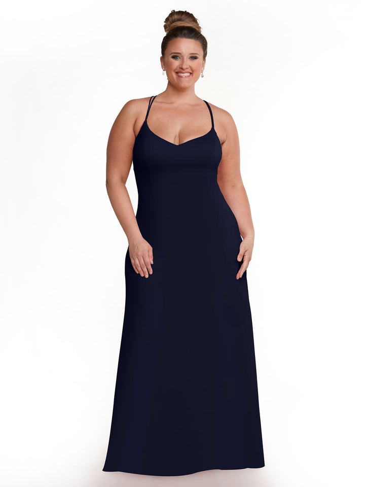 A woman with light skin and brown hair in a bun is wearing the Avery Austin 83045 navy A-Line dress with spaghetti straps, standing and smiling against a plain white background.