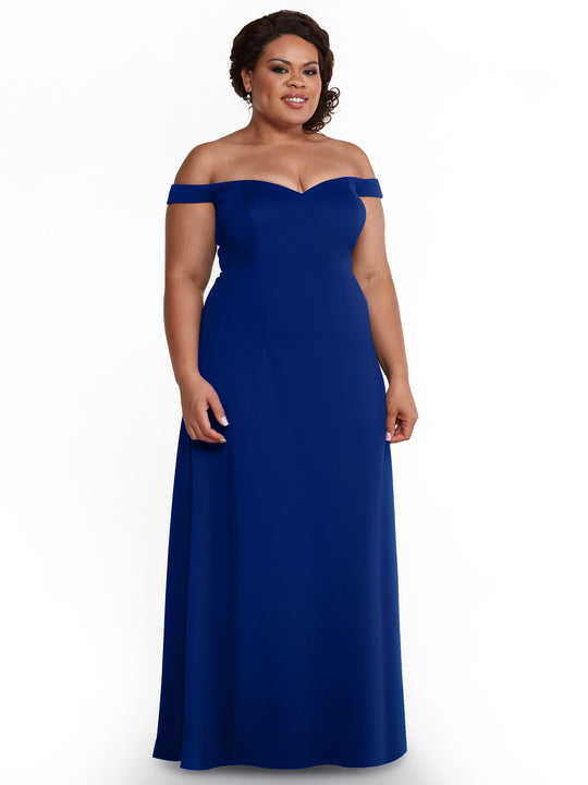 A woman in Avery Austin’s royal A-Line dress (Style 83049) stands against a white background, her curly hair up and a gentle smile on her face.