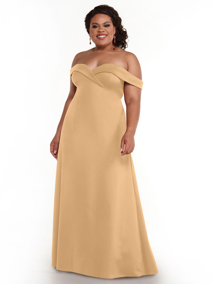 A woman smiles in the Avery Austin 83050, an off-the-shoulder, floor-length A-Line dress in Bisque with a fitted bodice and flared skirt, standing against a plain white background.