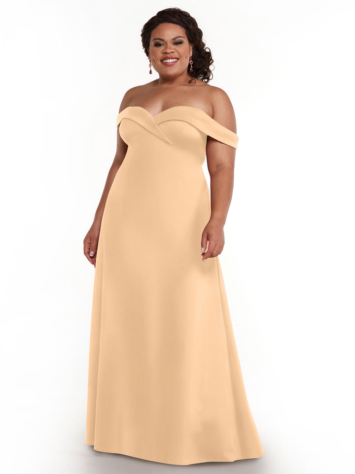 A woman smiles against a white background wearing Avery Austin’s blush, off-the-shoulder, floor-length A-Line dress (style 83050), her hair in loose curls and accessorized with earrings.