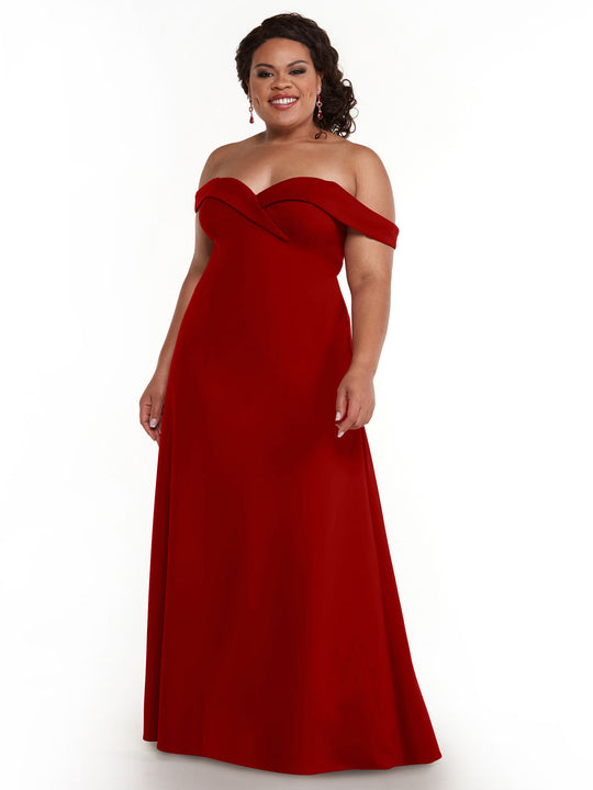 A woman wearing the Avery Austin 83050, an elegant off-the-shoulder A-line gown in Ruby, stands smiling against a white background with her curly hair styled back and accessorized with dangling earrings.