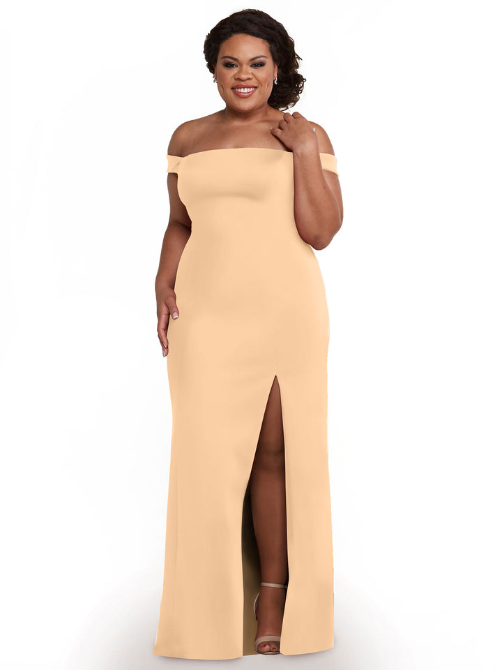 A woman smiles in the Avery Austin 83052 off-the-shoulder bridesmaid dress, a floor-length blush gown with a thigh-high side slit, pairing it with heeled sandals as she touches her hair and rests one hand at her side.