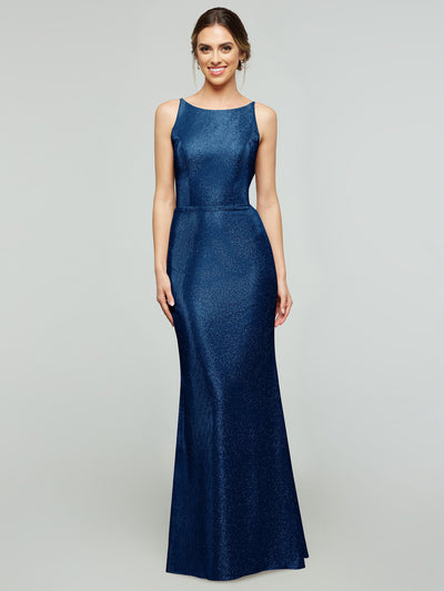 A woman smiles in the averyaustin 84001 - Tried On Sample, a sleeveless, floor-length Glitter Sapphire knit evening gown with a fitted bodice and flared skirt, posed against a light gray background.