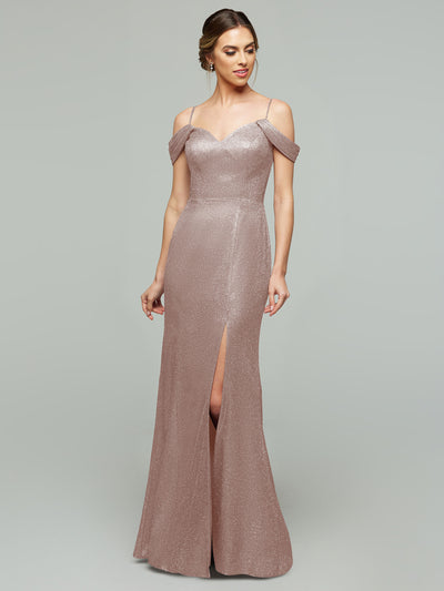 A woman models the averyaustin 84002 - Tried On Sample, a Glitter Blush, glitter knit off-the-shoulder floor-length dress with a thigh-high slit against a light-gray background.