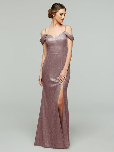 A woman models the averyaustin 84002 - Tried On Sample: a shimmering mauve glitter knit off-the-shoulder dress with spaghetti straps and a thigh-high slit, standing before a plain light gray background.
