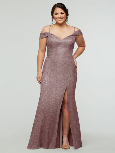 A woman smiles with her hands in the pockets of the averyaustin 84002 - Tried On Sample, a glitter rose gold off-the-shoulder dress with a thigh-high slit and floor-length hem, standing against a plain light background.