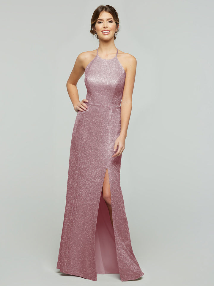 A woman smiles in the averyaustin 84005 - Tried On Sample, a sleeveless, floor-length Glitter Mauve knit sheath dress with a high neckline and thigh-high slit, posing against a plain light gray background.