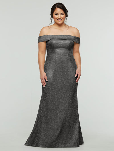 A woman models the averyaustin 84010 - Tried On Sample in Glitter Gun Metal, an off-the-shoulder, floor-length mermaid dress, standing against a light gray background and smiling with her hands at her sides.