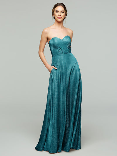 A woman models the averyaustin 84012 - Tried On Sample in Glitter Teal, an A-line strapless gown with pockets and subtle shimmer. She smiles slightly with her hair up and minimal jewelry, standing against a plain light gray background.