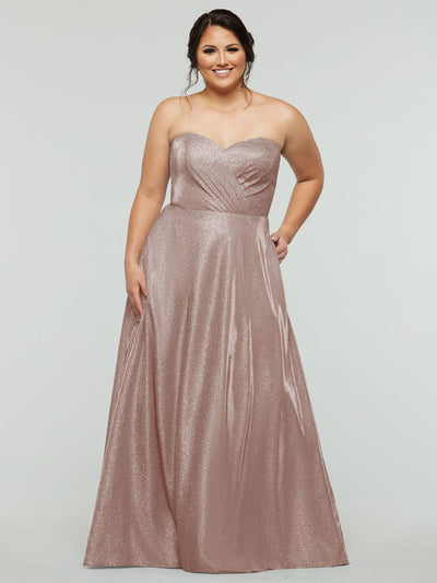 A woman in the 84012 - Tried On Sample by averyaustin, a strapless Glitter Blush A-Line gown with a sweetheart neckline, smiles against a light gray background—perfect inspiration for stunning sample dresses.