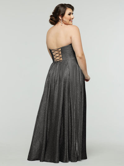 A woman models the Avery Austin 84014 - Tried On Sample gown, featuring sparkly fabric and a corseted back, as she faces away and smiles over her shoulder against a plain light background.