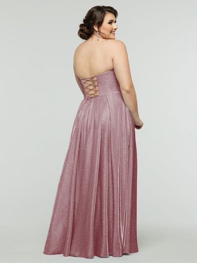 A woman in the floor-length, sparkling pink 84014 - Tried On Sample gown by averyaustin stands facing away, smiling over her shoulder. The strapless dress with a corseted back shimmers against the plain, light background.