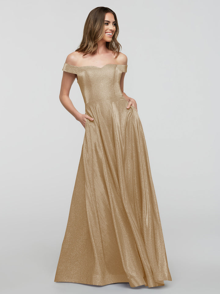 A woman smiles in the averyaustin 84020 - Tried On Sample gown, featuring an off-the-shoulder A-line silhouette and pockets in glitter champagne, posing against a plain light background—ideal for sample dresses.