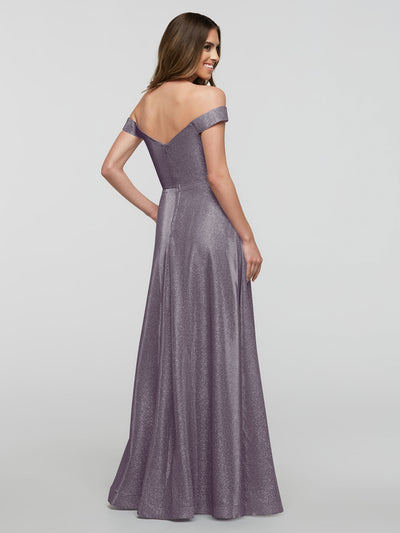 A woman smiles over her shoulder in the averyaustin 84020 - Tried On Sample, an off-the-shoulder A-line gown in shimmery lavender, set against a simple, light background that highlights the dress's elegance.