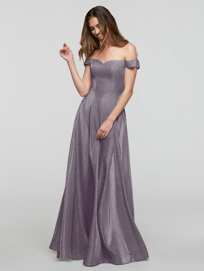A woman smiles and looks down with one hand raised, modeling the averyaustin 84020 - Tried On Sample: an A-Line, off-the-shoulder, floor-length shimmery lavender gown against a plain background.