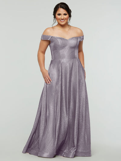 A woman smiles against a plain light background in the averyaustin 84020 Tried On Sample, a floor-length Glitter Dusty Lavender A-Line gown with a fitted bodice, flowing skirt with pockets, and elegant off-the-shoulder sleeves.